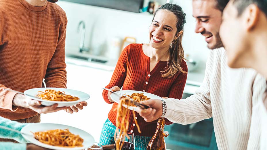 Happy group of friends eating spaghetti at home dinner party
