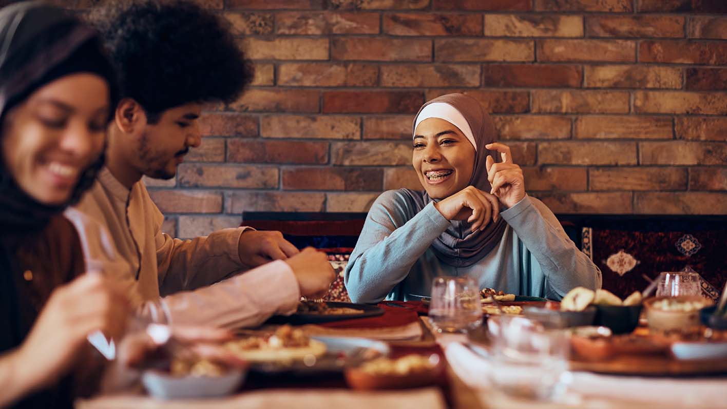 Young happy woman talking to her friends while having lunch together at dining table