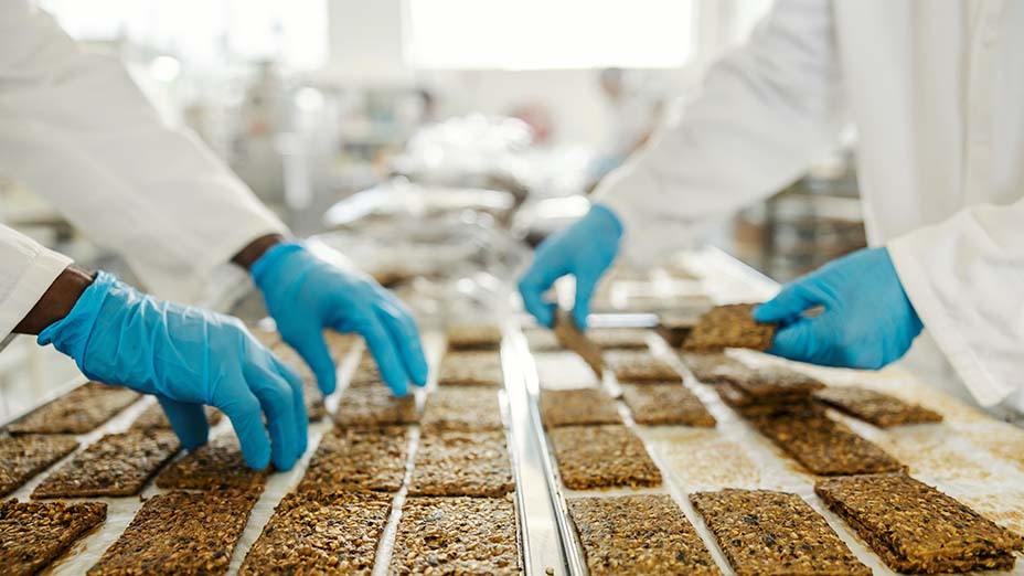 Cropped picture of food factory workers' hands collecting freshly baked biscuits from tray.