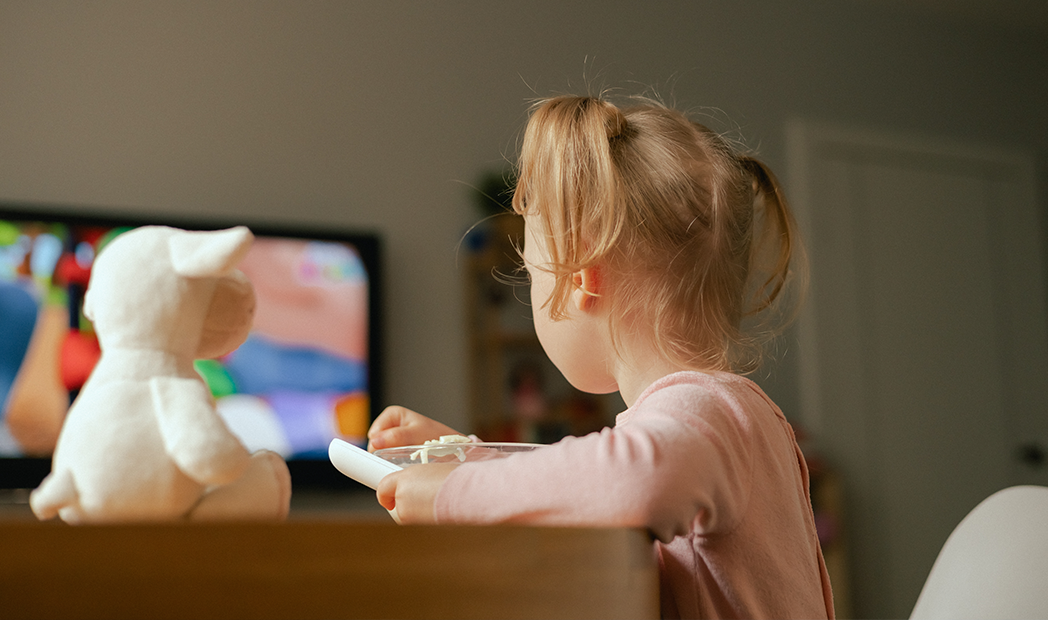Baby girl eats breakfast and watches cartoons on TV