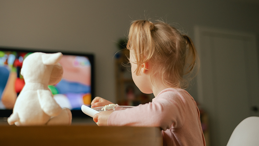 Baby girl eats breakfast and watches cartoons on TV