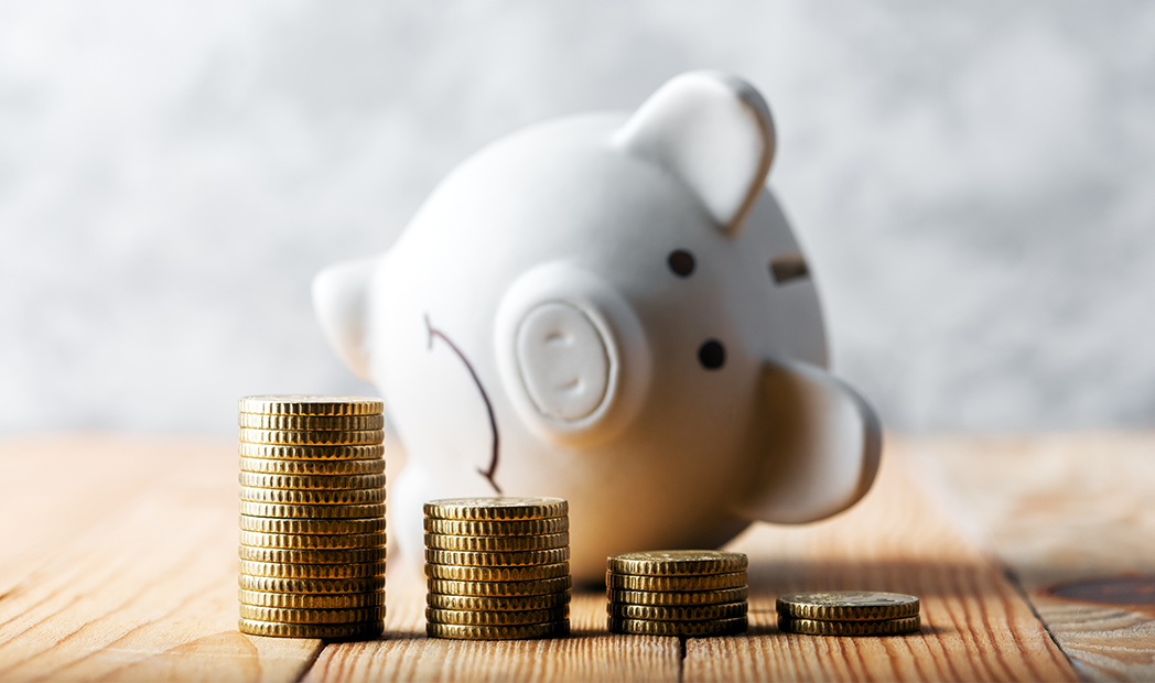 sad piggy bank behind stacks of coins symbolizing the fall of monetary assets