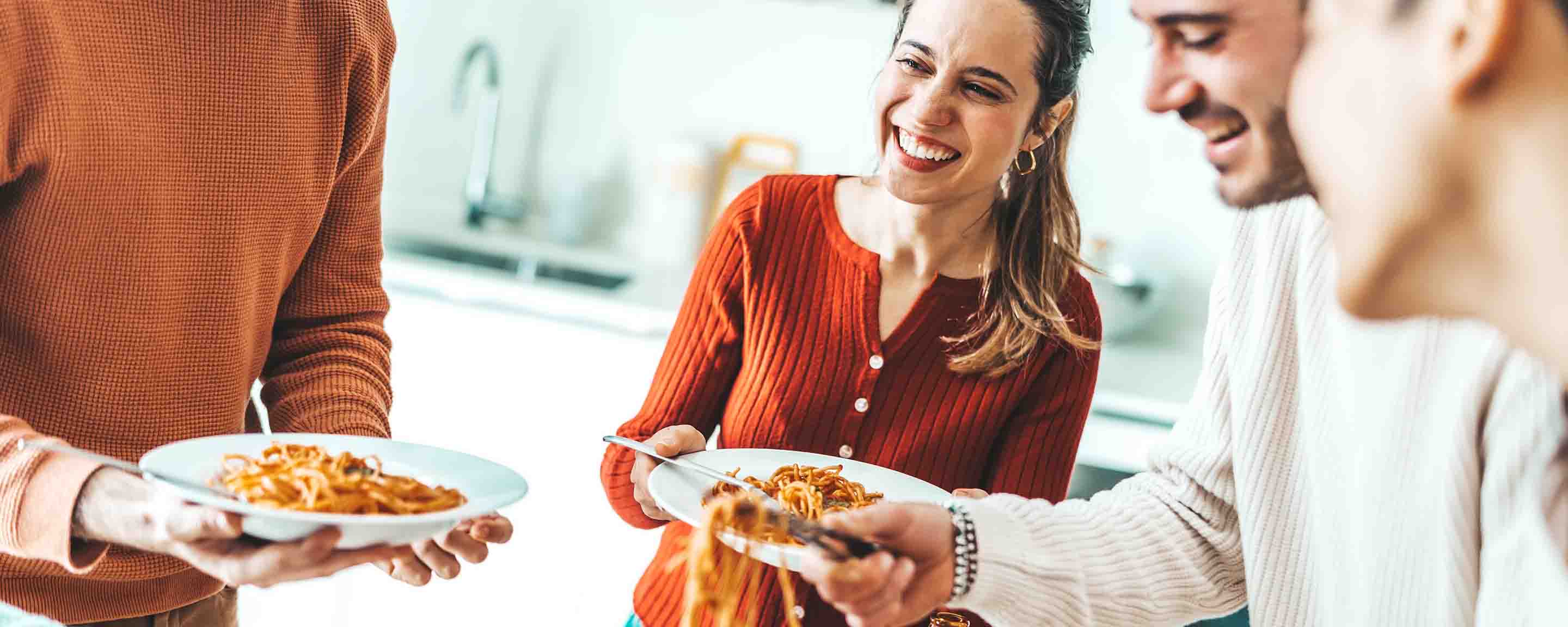 Happy group of friends eating pasta at home dinner party