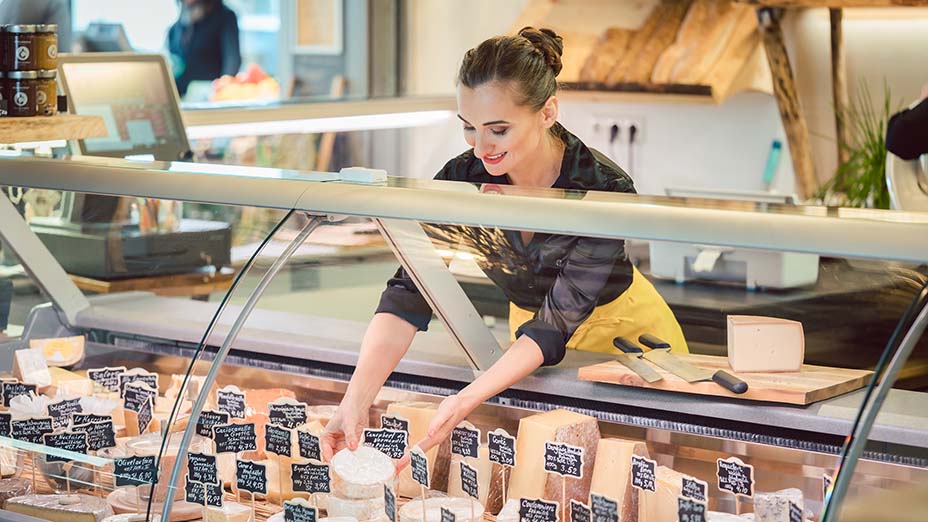 female shop clerk sorting cheese in supermarket display