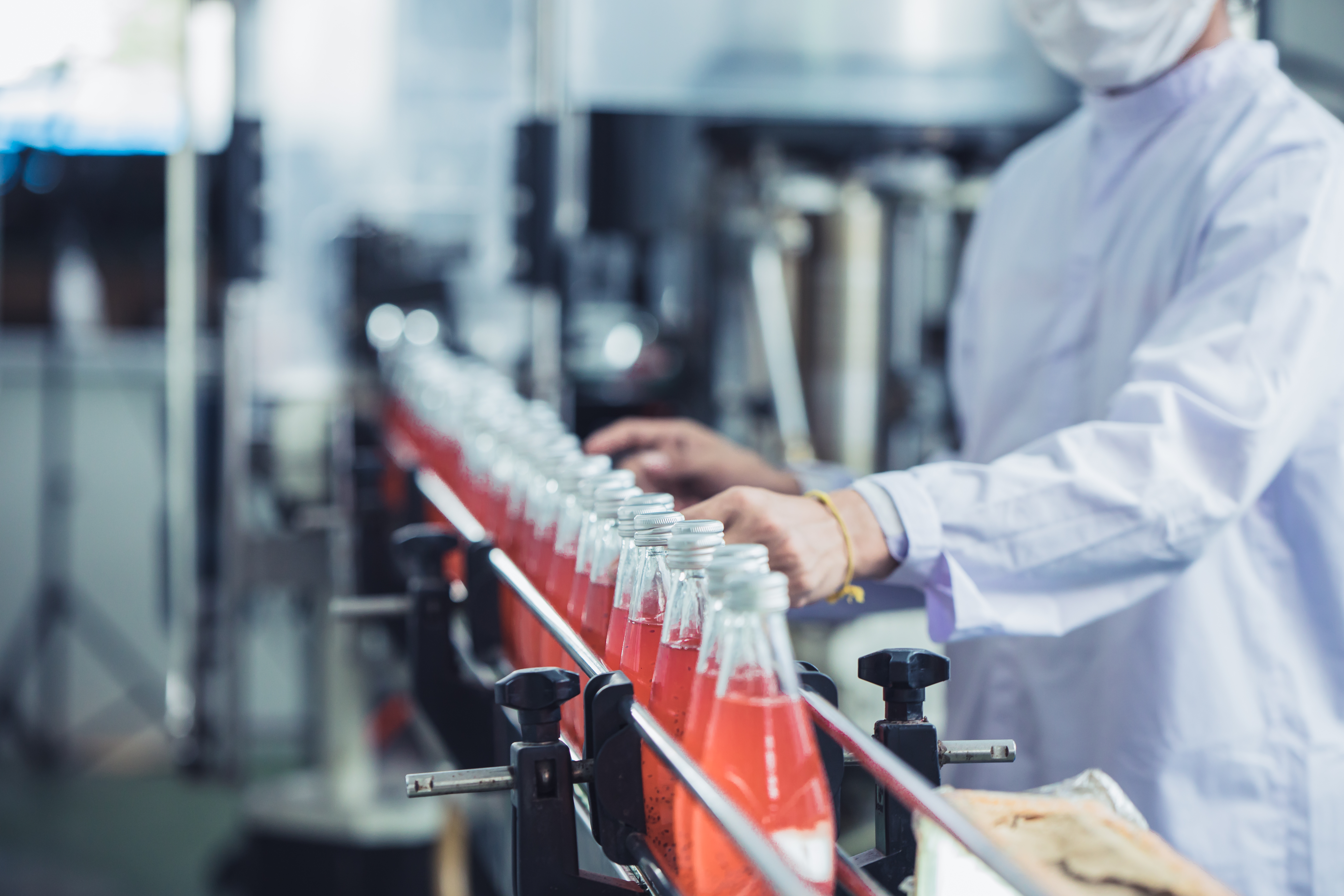hygiene worker checking glass bottled juice on production line 